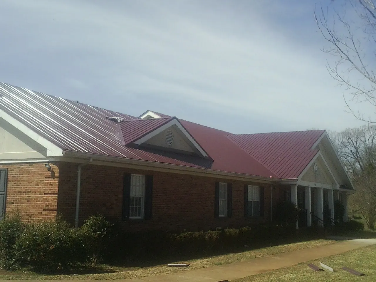 Red metal roof with gabled entries on a long brick building, from a Hail Damage Roof Repair job in Denmark